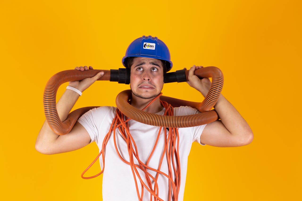 Man with blue helmet and orange hoses looks confused against a bright yellow background.